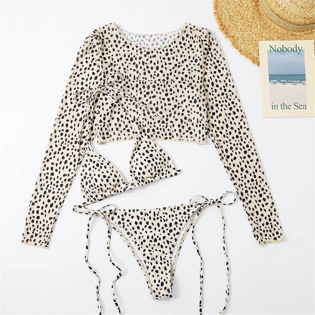 An elegant three-piece swimwear featuring a bold leopard print, long-sleeve top, and matching bikini set, designed for a feminine yet confident and stylish beach look
